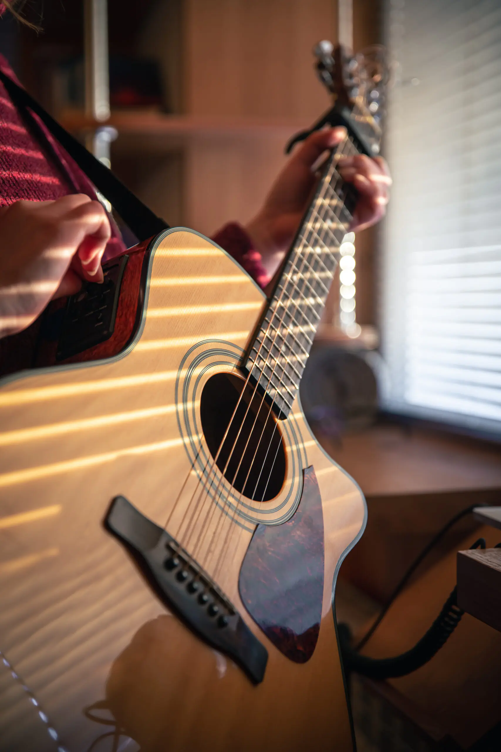 A girl with an acoustic guitar in the sunlight, through the blinds, early in the morning.