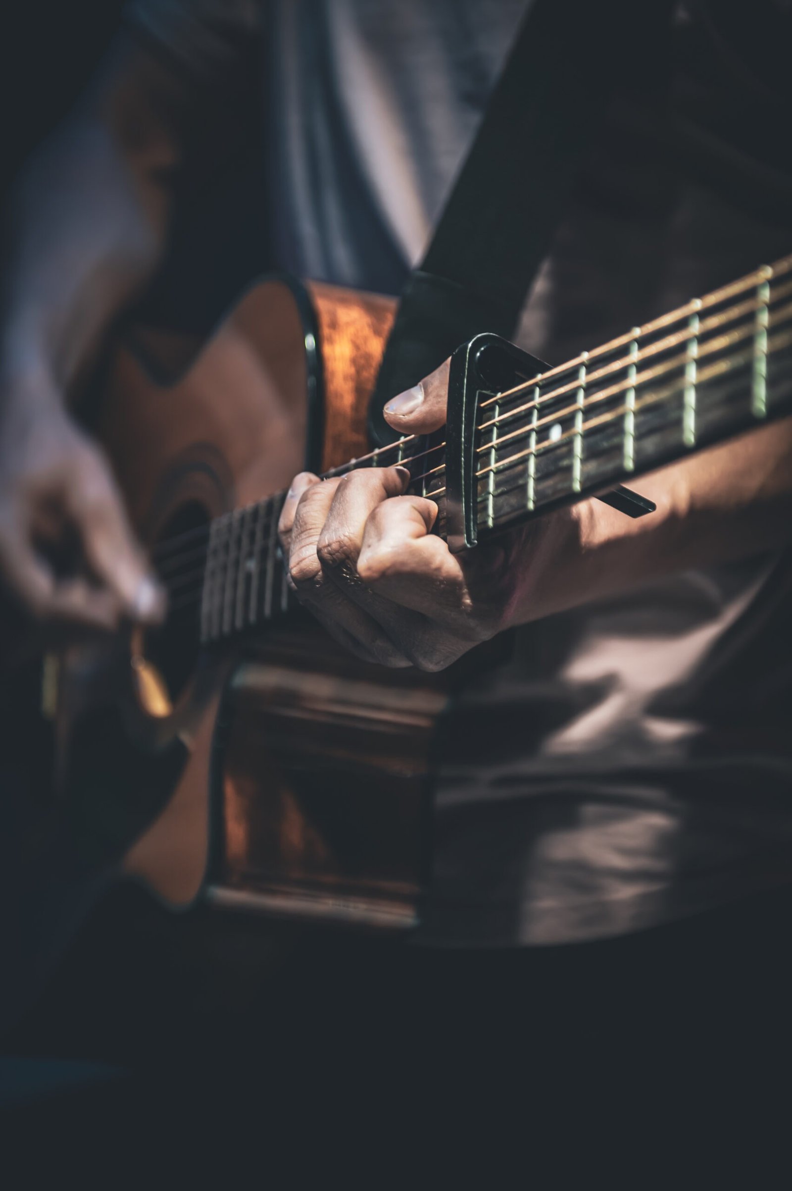 A man plays an acoustic guitar in the dark, close-up.